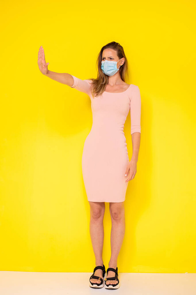 you can be fashion but wear a mask for virus protection. woman in elegant dress posing on yellow and stopping the clouse contact - Foto, Imagen