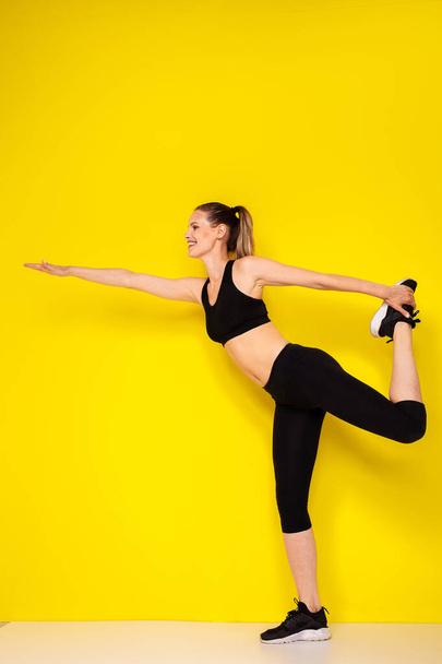 strech your muscle before the sport exercise. young athletic woman in sportwear outfit doing streching on yellow background - Photo, image