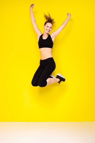 you jump when you are happy. athletic woman in sportwear jumping on yellow background - Fotoğraf, Görsel
