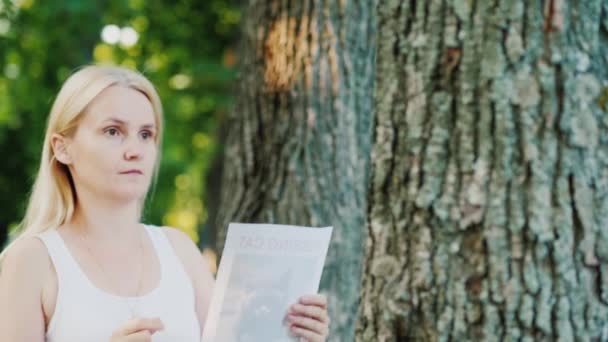 Young woman attaches an ad to a tree in the park - Filmmaterial, Video