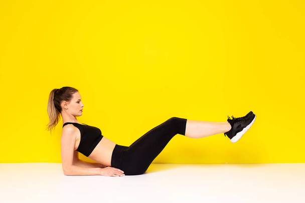 athletic woman in sportwear execise her abs, doing some sport exercise on the floor for the hips and abs, on yellow background - 写真・画像