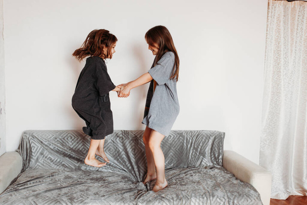 Two little girls, sisters playing at home, jumping on the couch, hugging, kissing each other, fighting, arguing, isolation, vacation, weekend at home, communication - Фото, изображение