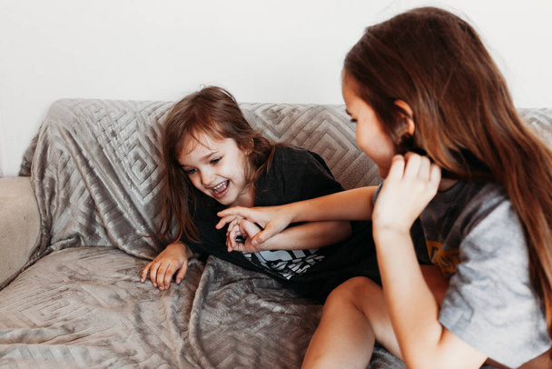 Two little girls, sisters playing at home, jumping on the couch, hugging, kissing each other, fighting, arguing, isolation, vacation, weekend at home, communication - Photo, image