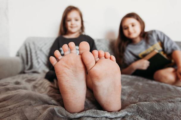 Two little girls, sisters playing at home, jumping on the couch, hugging, kissing each other, fighting, arguing, isolation, vacation, weekend at home, communication, legs - Foto, imagen