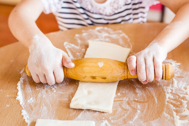 A girl and little sister are cooking pastries in the kitchen at the table, flour and rolling pin, cooking with children, delicious food, junk food, carbohydrates, breakfast, croissants - Foto, Bild