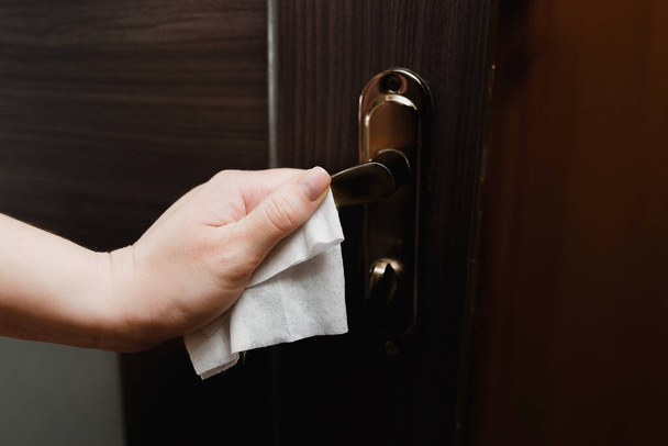 Een close-up van de hand van een man houdt een deurkruk door een servet. Bescherming tegen contact met oppervlakken op openbare plaatsen tijdens de Kovid-19 pandemie. Quarantaineconcept - Foto, afbeelding