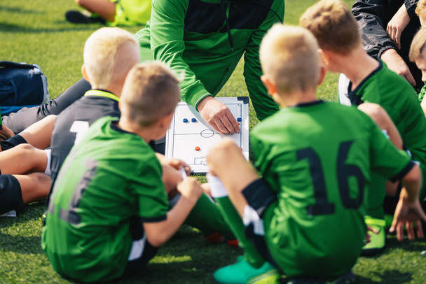 Fiatal fiúk a focicsapatban hallgatják az edzőt. Az edző oktatást ad a gyerekeinek focicsapatnak. Foci bajnokság. Iskolai foci verseny. Coach segítségével Tactics Board, hogy elmagyarázza a játék stratégia - Fotó, kép