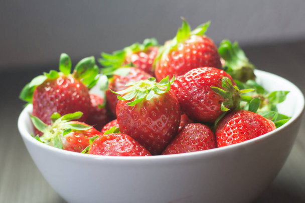 Séance photo de fraises bio fraîches. Il comprend également des textures en bois gris et un bol blanc. La combinaison de couleurs vives se distingue
. - Photo, image