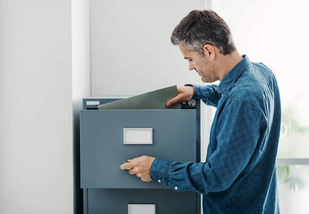 Office clerk searching files in the filing cabinet, he is looking into the file drawer - Fotoğraf, Görsel