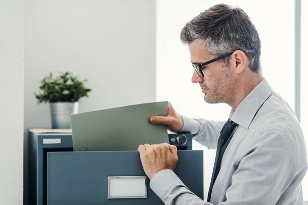 Businessperson at work: professional confident office clerk searching files in the filing cabinet - Foto, imagen