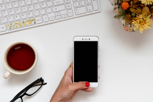 Dívka ruka drží bílý smartphone v kanceláři doma při dojíždění. Plochá perspektiva, pohled shora - Fotografie, Obrázek