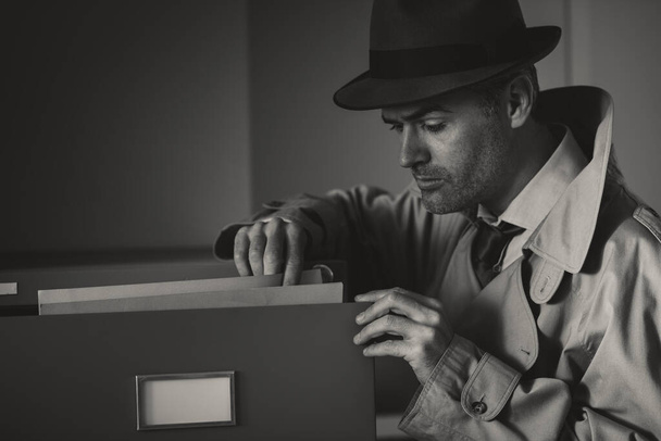 Vintage undercover criminal spy stealing files in a filing cabinet late at night, security and data theft concept - Foto, afbeelding