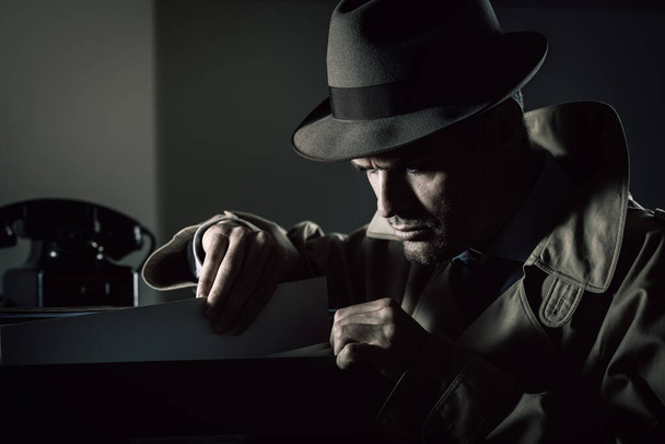 Vintage undercover criminal spy stealing files in a filing cabinet late at night, security and data theft concept - 写真・画像