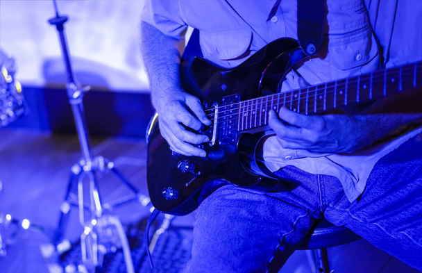 Homem tocando guitarra no palco closeup iluminado em luz azul
 - Foto, Imagem