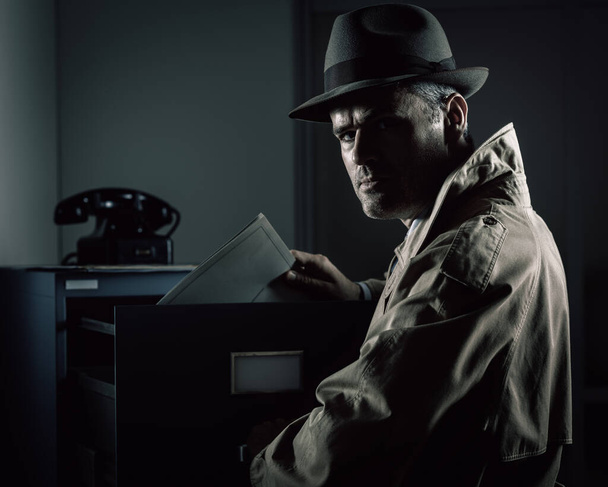 Vintage undercover spy stealing files in a filing cabinet late at night, security, data theft and crime concept - Photo, Image