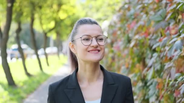 Attractive young business woman in a black jacket and glasses walks and walks along the street outdoors. - Кадри, відео