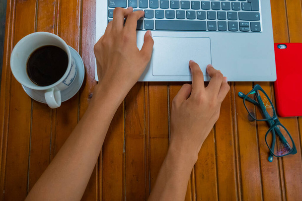 Руки с помощью ноутбука на деревенском деревянном столе с кофейной чашкой, очками и мобильным телефоном
 - Фото, изображение