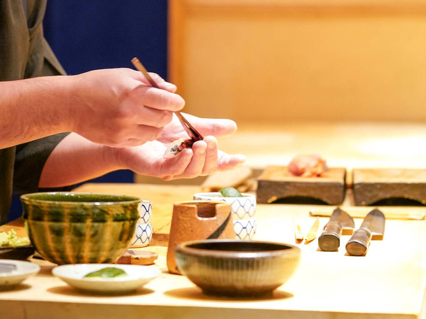 Szef kuchni szczotkuje sos shoyu na surowej rybie. Ciesz się doświadczeniem Omakase w japońskiej restauracji sushi. - Zdjęcie, obraz