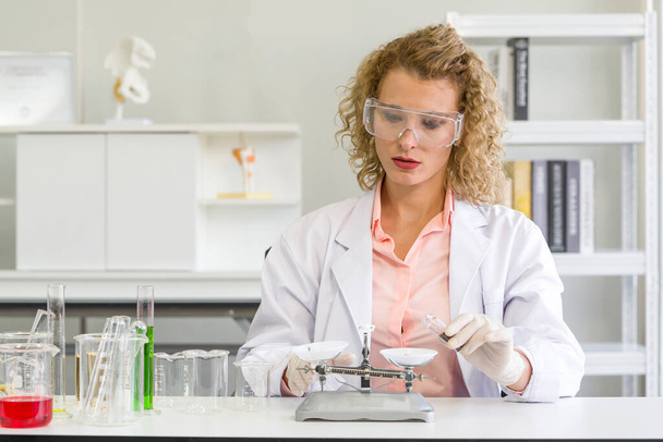 A young blonde scientist is measuring the chemicals for an experiment. Working atmosphere in chemical laboratory. Test tubes and beakers filled with chemicals on the table. - Photo, Image