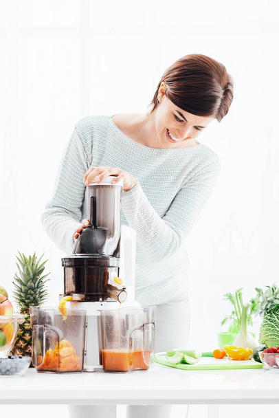 Young smiling woman using a juice extractor and preparing an healthy smoothie using fresh organic vegetables and fruit - Fotoğraf, Görsel