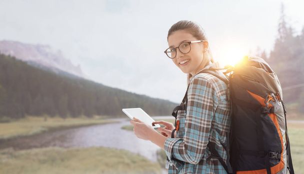 Young smiling woman trekking in nature on the mountains and connecting with a digital tablet - Photo, image