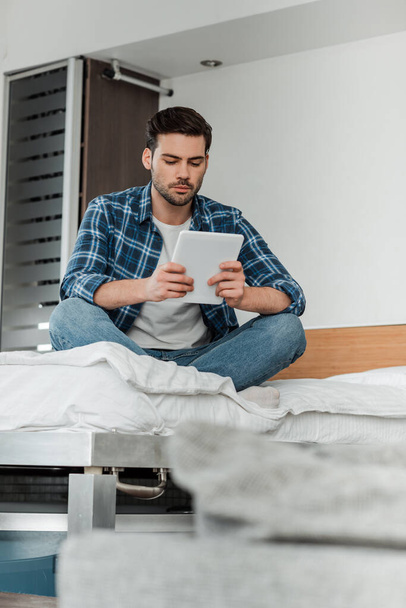 Selective focus of man with crossed legs using digital tablet on bed  - Photo, Image