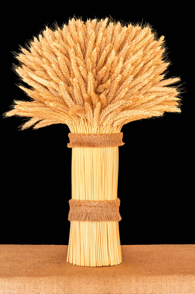 sheaf of ripe wheat standing on a table close-up on a dark background - Photo, Image