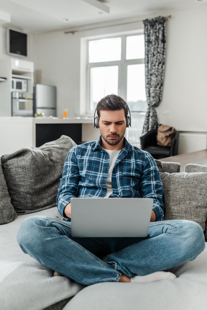 Freelancer listening music in headphones and using laptop on couch at home  - Photo, Image