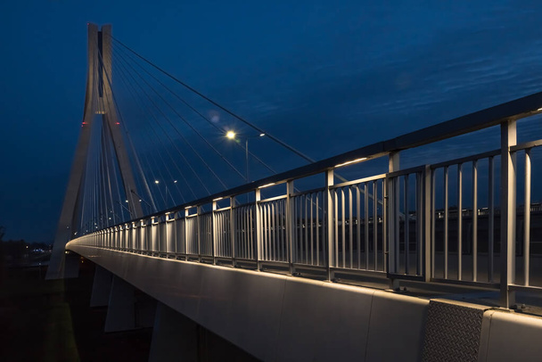 Akşamları mavi gökyüzü ve bulutlardan oluşan bir arkaplan karşısında kablo destekli köprü. - Fotoğraf, Görsel