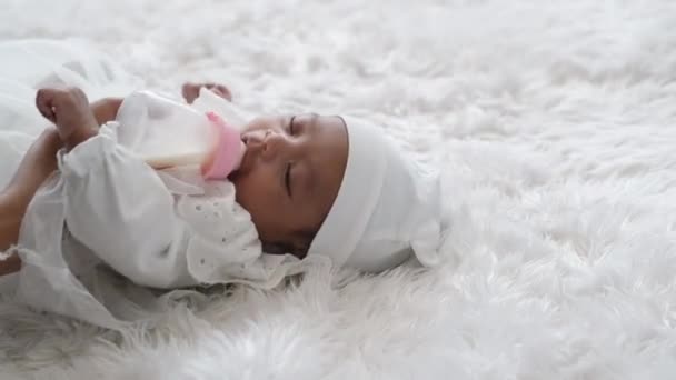 Da vicino il piccolo neonato mangia il latte dalla bottiglia e si sdraia sul letto bianco con la luce del giorno
. - Filmati, video
