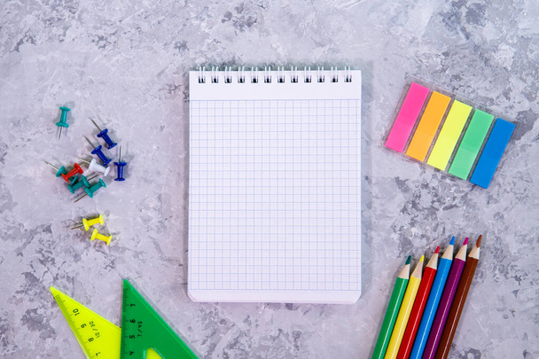 A set of stationery. Notepad, colored pencils, stationery buttons and multicolored stickers on a gray background. Space for text, background. Flat lay, top view - Φωτογραφία, εικόνα