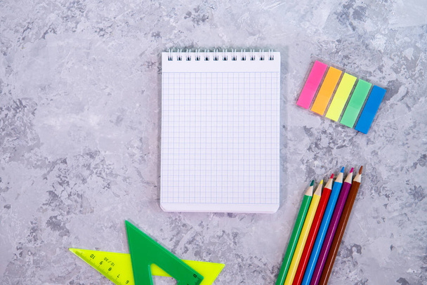 A set of stationery. Notepad, colored pencils, multi-colored stickers on a gray background. Space for text, background. Flat lay, top view - 写真・画像