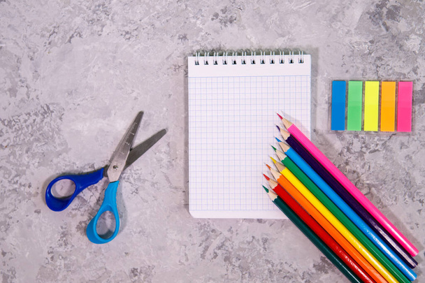 A set of stationery. Notepad, colored pencils, scissors and multi-colored stickers on a gray background. Space for text, background. Flat lay, top view - Foto, Imagen