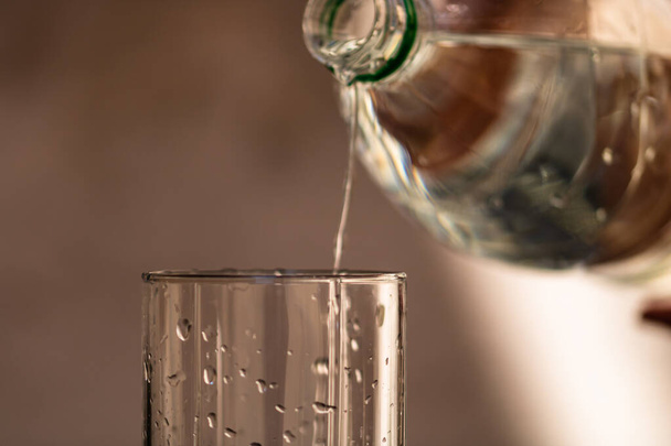 Pouring water from plastic bottle into a glass on blurred background. Selective focus and copy space - Fotó, kép
