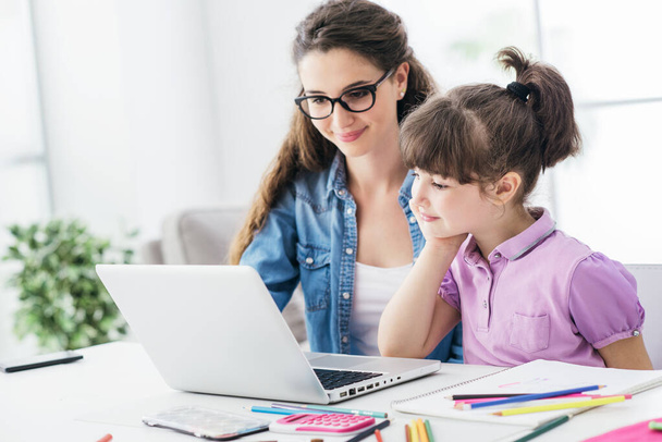 Young teacher and cute girl using a laptop together and connecting online, technology and entertainment concept - Photo, image
