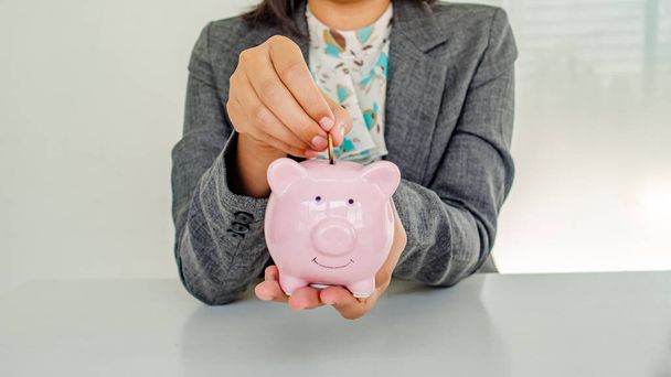 A business successful person is putting the coins in a piggy bank while working in the office. saving money is an investment for the future. Banking investment.  - Foto, immagini