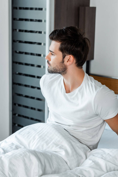 Handsome man looking away while sitting on bed  - Foto, imagen