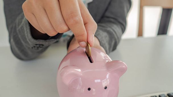 A business successful person is putting the coins in a piggy bank while working in the office. saving money is an investment for the future. Banking investment.  - Foto, Bild