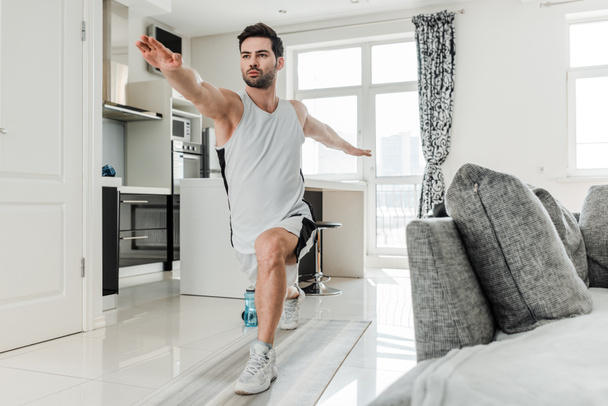 Handsome man in sportswear doing lunges while training at home  - Fotó, kép