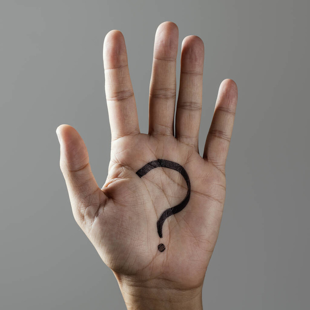 Nahaufnahme der Hand eines Mannes mit einem Fragezeichen in seiner Handfläche, auf grauem Hintergrund - Foto, Bild