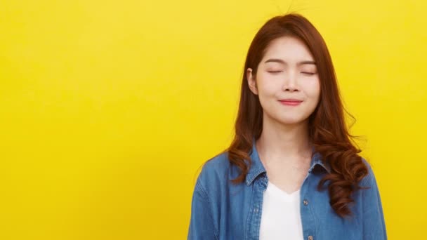 Porträt einer jungen Asiatin, die mit heiterem Gesichtsausdruck lächelt, etwas Erstaunliches in legerer Kleidung zeigt und vor gelbem Hintergrund in die Kamera blickt. Gesichtsausdruck.  - Filmmaterial, Video