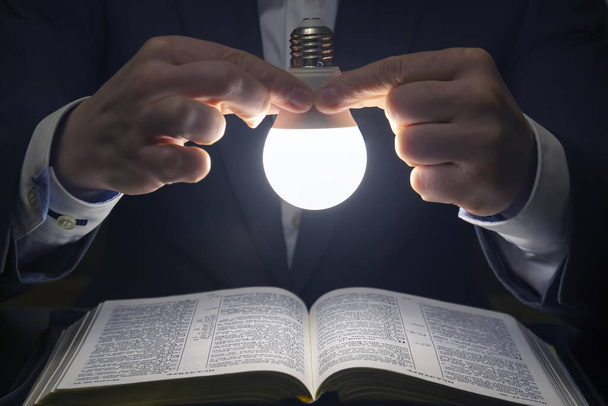 hombre lee la sagrada Biblia a la luz de la lámpara led encendida. la búsqueda de Dios y el estudio del libro. Cristianismo y religión
 - Foto, imagen