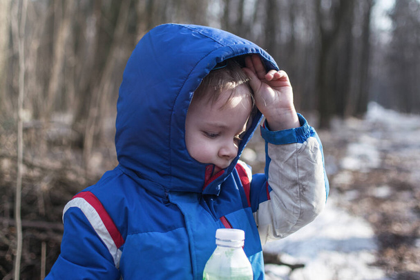 Mały chłopiec na spacerze trzyma plastikową butelkę w lesie.. - Zdjęcie, obraz