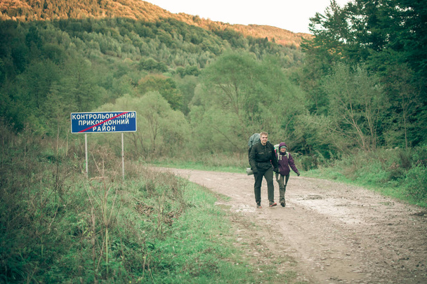 Carpathians, Ukraine- September 29, 2018: A man and a woman with backpacks are walking along a mountain road. - Photo, image