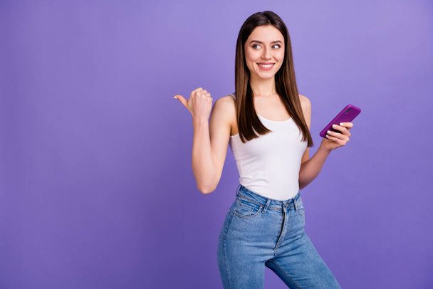 Photo of attractive interested lady hold telephone direct thumb finger empty space advising sale technologies prices wear white singlet jeans isolated pastel purple color background - Φωτογραφία, εικόνα