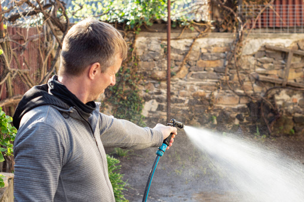 Man watering backyard lawn using hosepipe in sunny day - Photo, Image