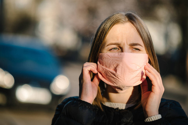 Girl with mask during COVID-19 pandemic coughing or sneezing at the street. The dangers of Coronavirus. Risk of spreading infection. Covering nose and mouth. Woman cough in arm prevention. - 写真・画像