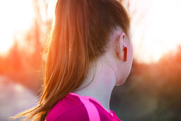 Молода товста дівчина з бездротовими навушниками проходить вздовж стежки в променях сонячного світла
 - Фото, зображення