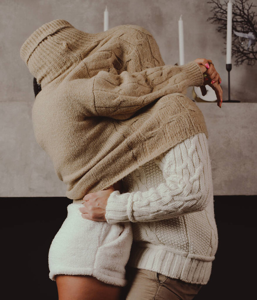  a couple in love in cozy sweaters in warm shades hid together under a sweater hugging. - Foto, Imagen