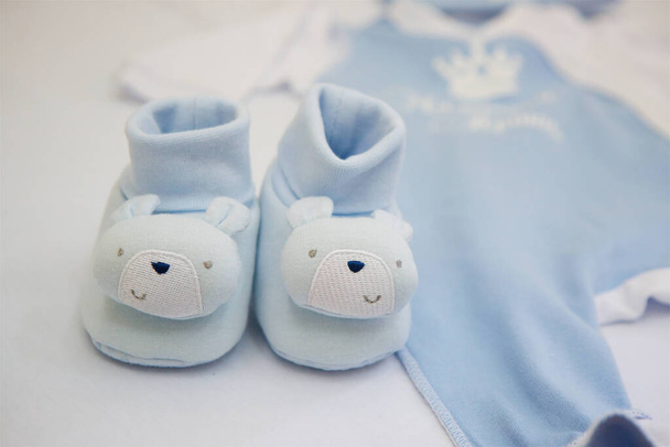 Kleine baby blauw met gezichten beren laarzen zijn op de tafel tegen de achtergrond van wazig kinderkleding. Het concept van wachten op een pasgeborene. - Foto, afbeelding